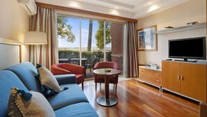 Un salon moderne avec un canapé, des fauteuils, un téléviseur et une vue dégagée grâce à de grandes fenêtres.