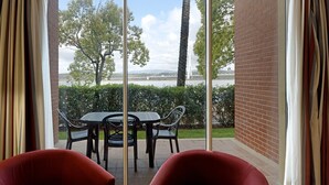 Un balcon avec une table et des chaises, une vue sur des arbres et un pont, et un mur en briques.