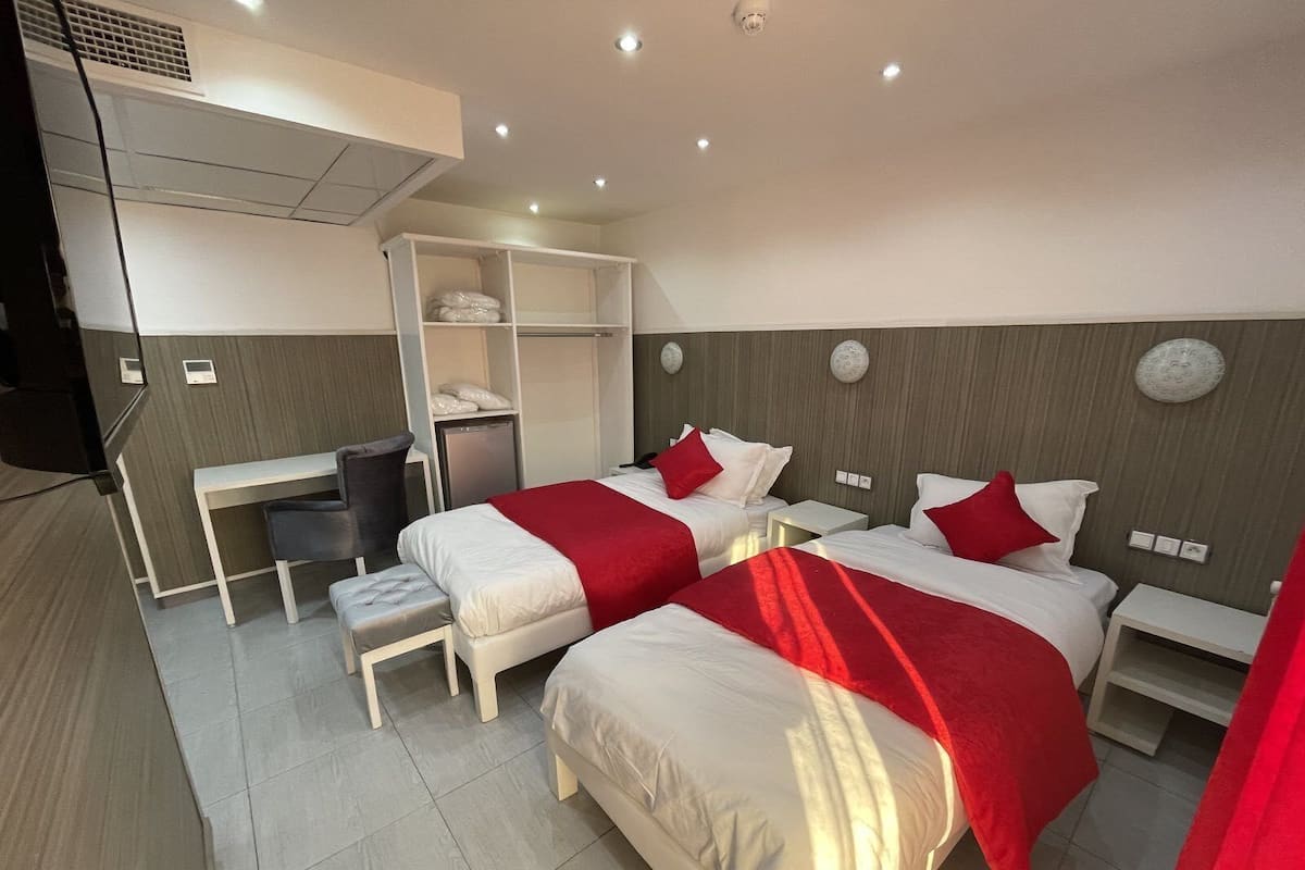 A hotel room with two beds, a desk, a chair, and a wardrobe.