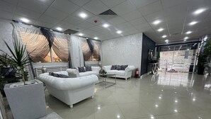A spacious lobby with white sofas, a marble coffee table, and a large potted plant. - Le Lido (Algiers)