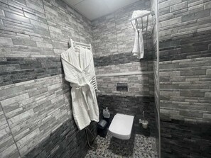 Et badeværelse med stenvæg, et hvidt badekar, et hvidt toilet og et bruseområde.