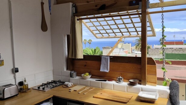 A kitchen with a wooden countertop, a gas stove, a toaster, and a window with a view of the sea and buildings.