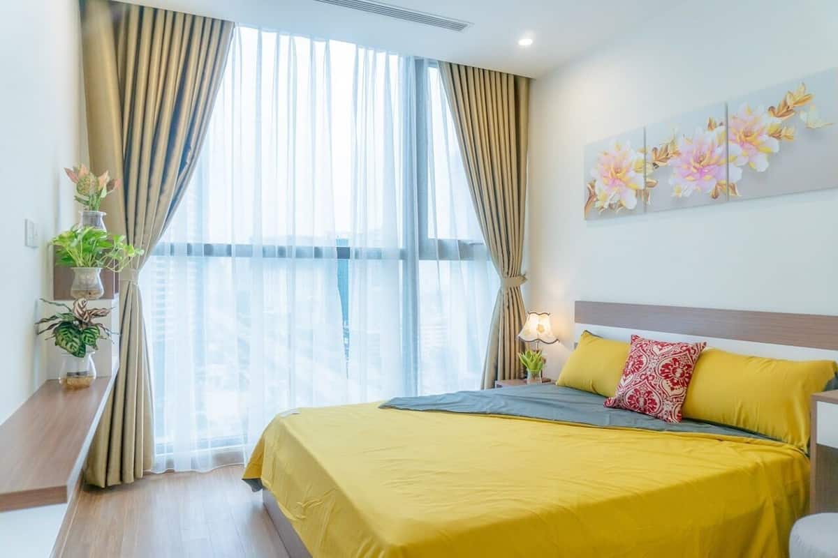 Ein Hotelzimmer mit Bett, Vorhängen, einem Fenster und einer Wand mit einem Blumenbild.