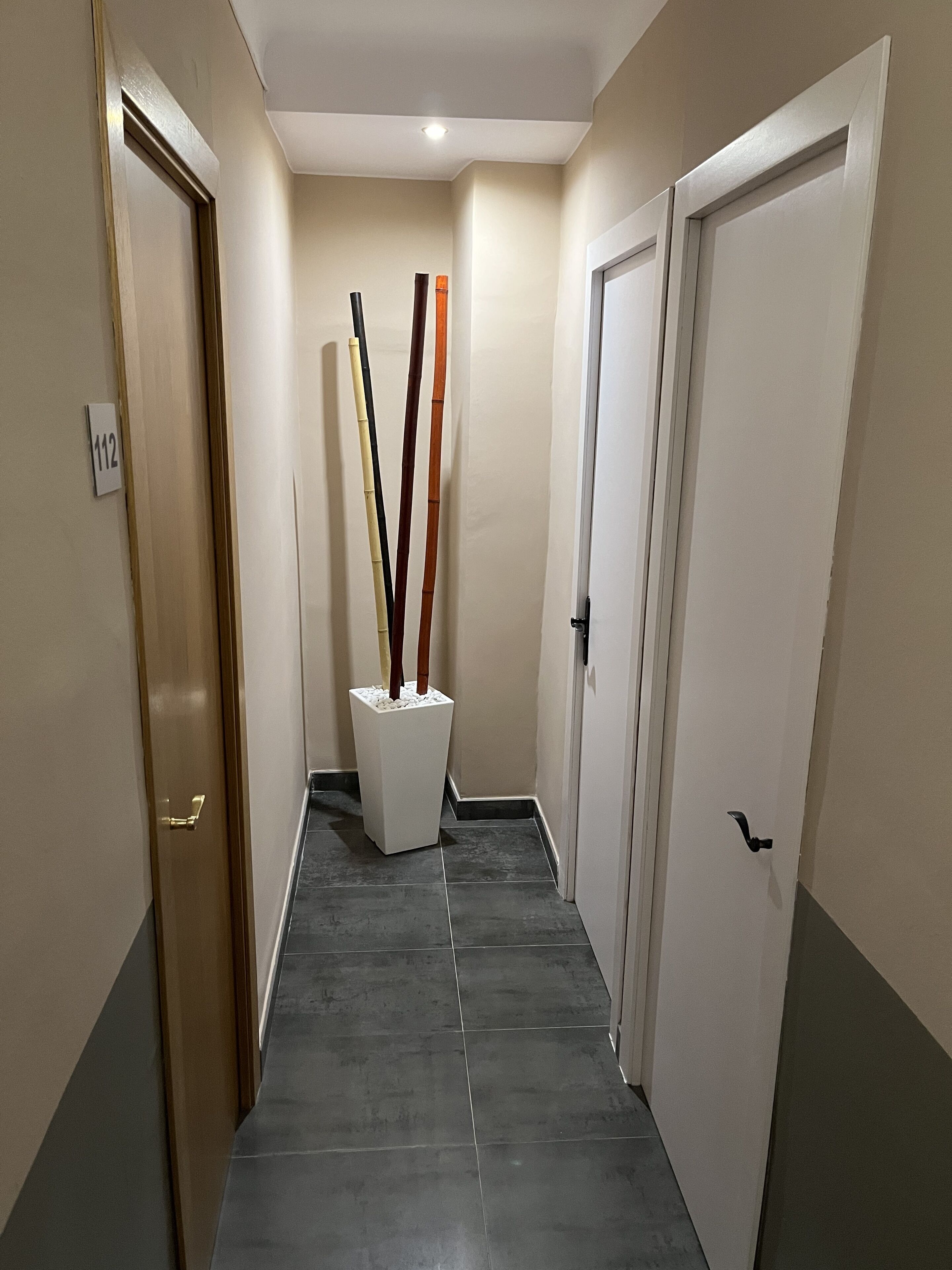 Un pasillo con piso de baldosas, un pilar blanco con palos y puertas a ambos lados.