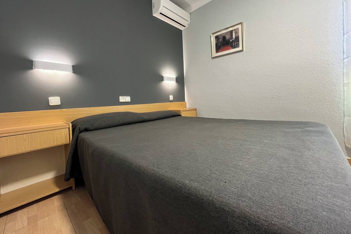 Un dormitorio con cama, mesitas de noche, unidad de aire acondicionado e iluminación en la pared.