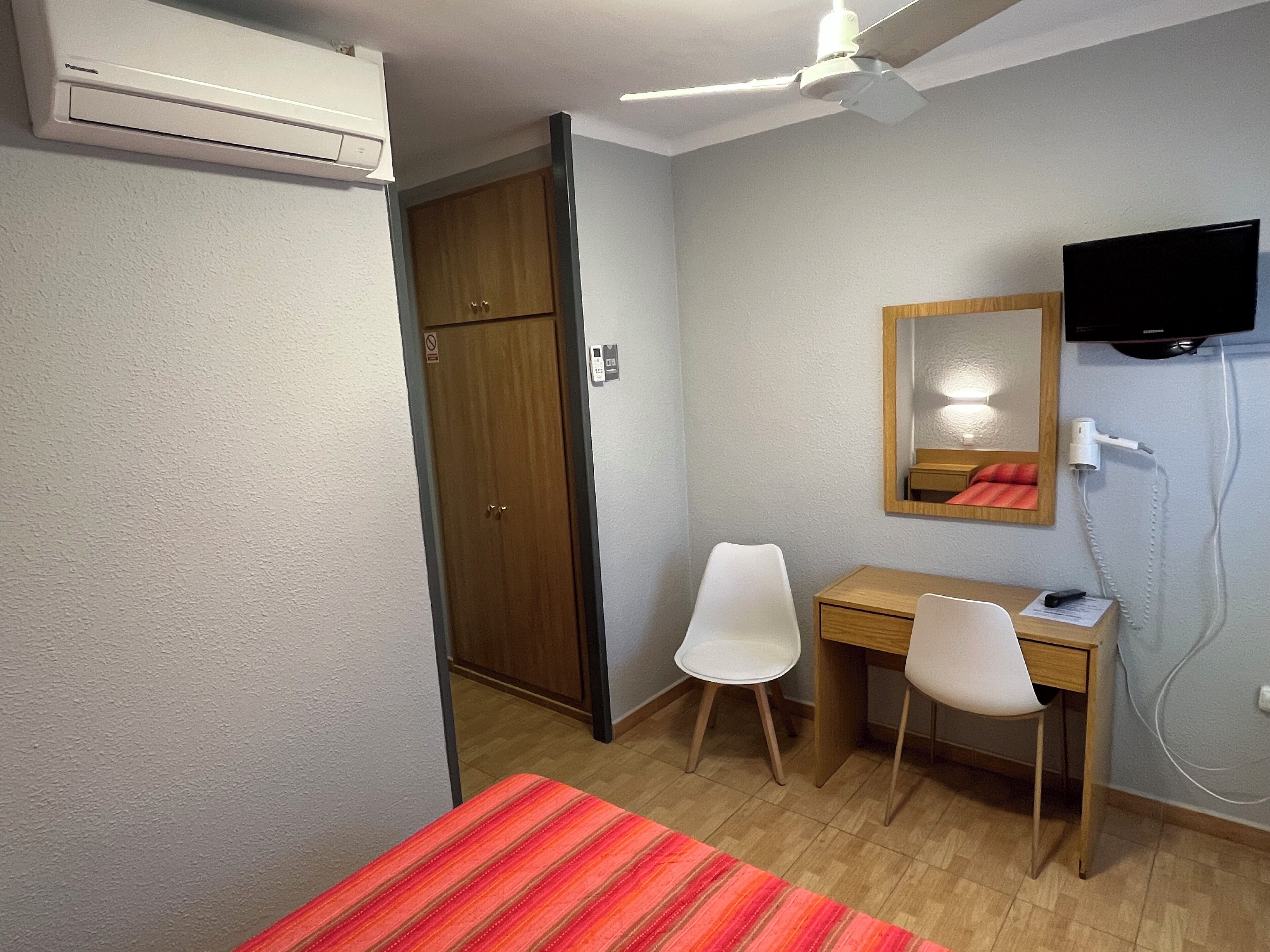 Una habitación de hotel con cama, escritorio, silla, televisor y armario.