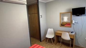 Una habitación de hotel con cama, escritorio, silla, televisor y armario.