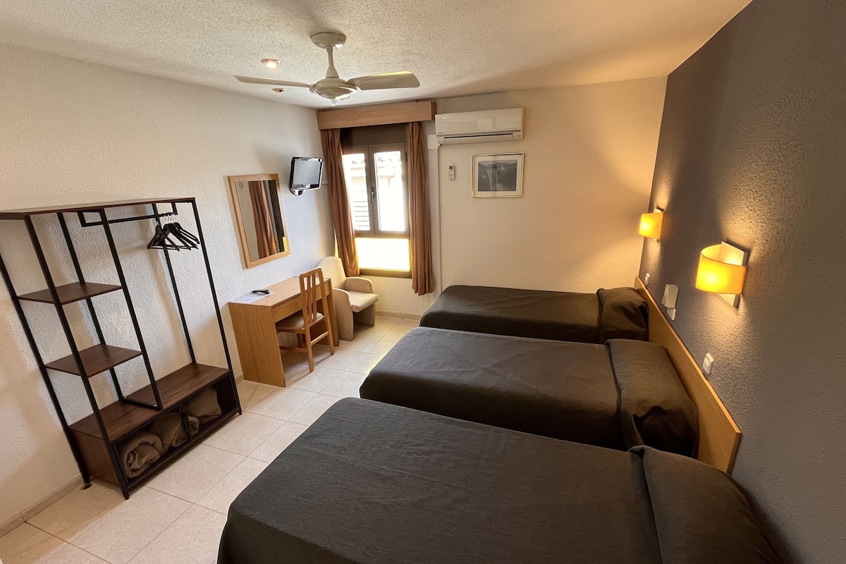 Habitación de hotel con dos camas, un escritorio, una silla, un armario, ventilador de techo, aire acondicionado e iluminación de pared.