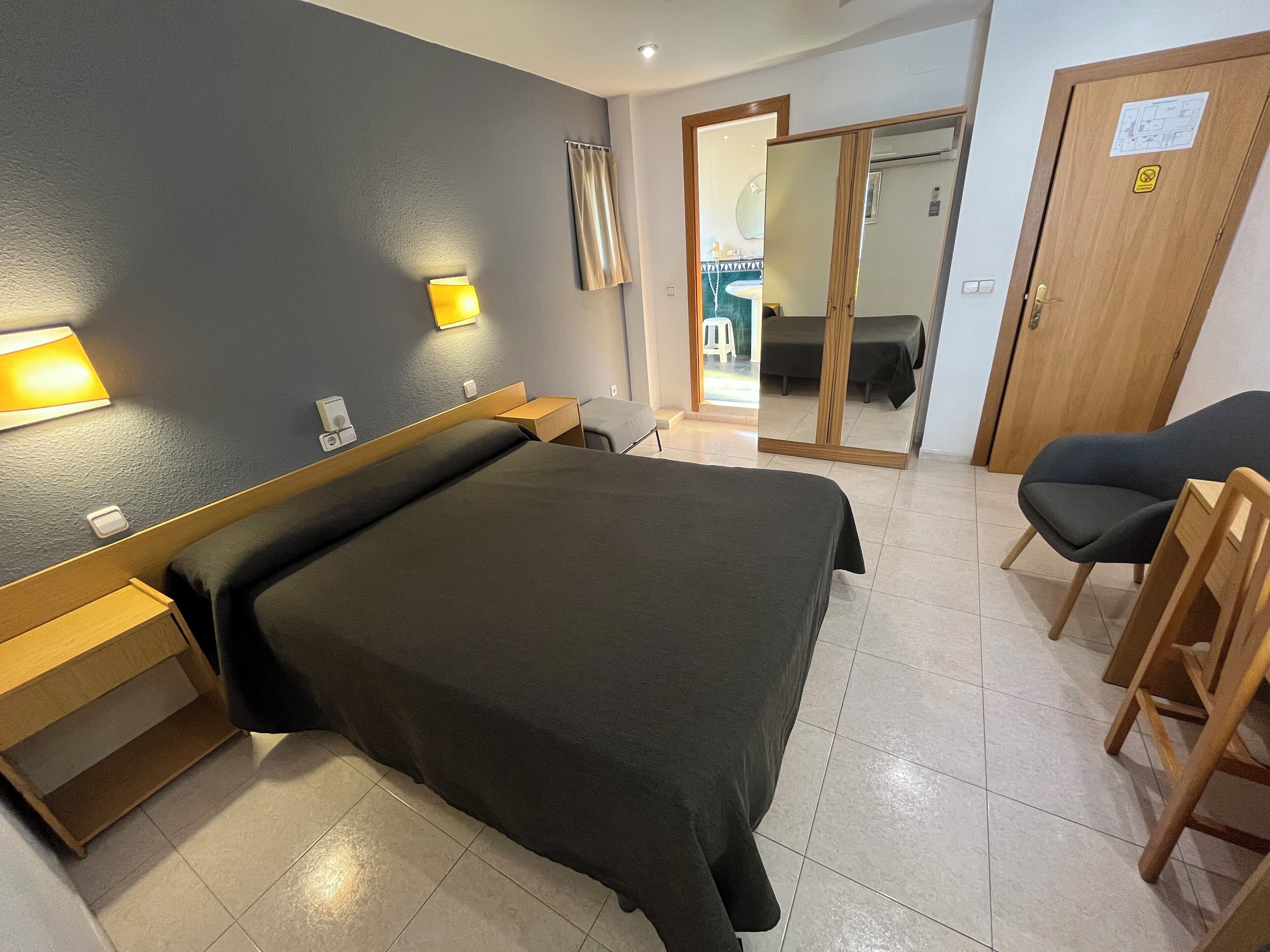 A hotel room with a large bed, bedside tables, a chair, and a mirror.