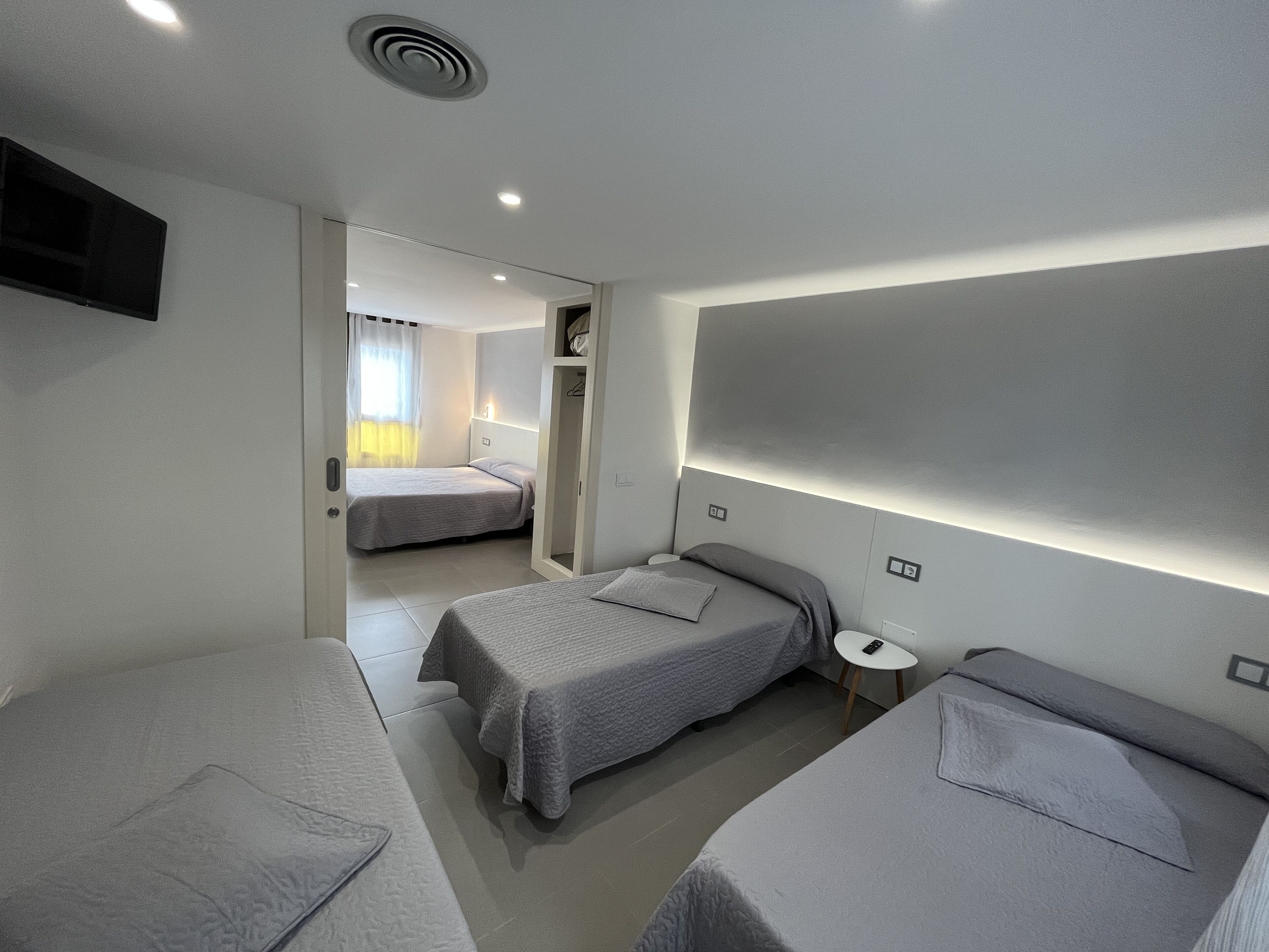 Una habitación de hotel moderna con dos camas individuales, una mesita y un televisor montado en la pared.