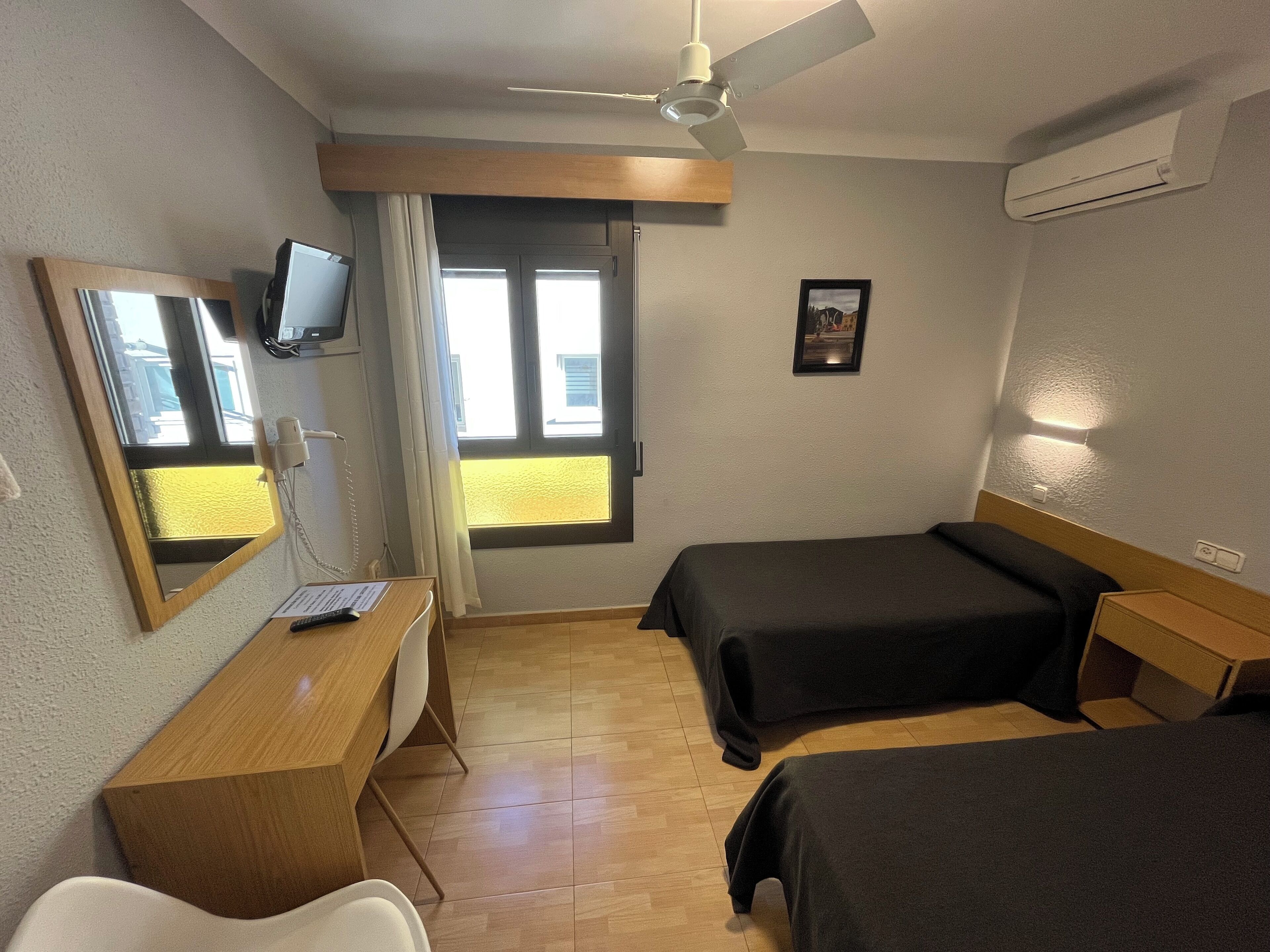 A hotel room with two beds, a desk with a chair, a television, and a window with curtains.