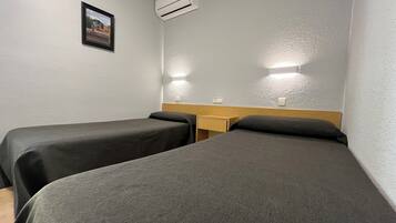 Een hotelkamer met twee eenpersoonsbedden, een houten nachtkastje, een airconditioningsysteem en een ingelijst foto aan de muur.