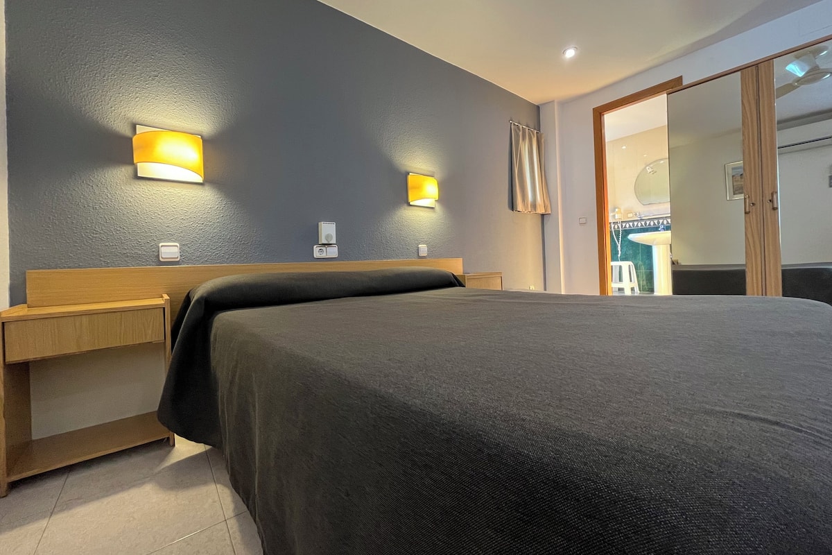 Una habitación de hotel con cama, mesitas de noche e iluminación en la pared.