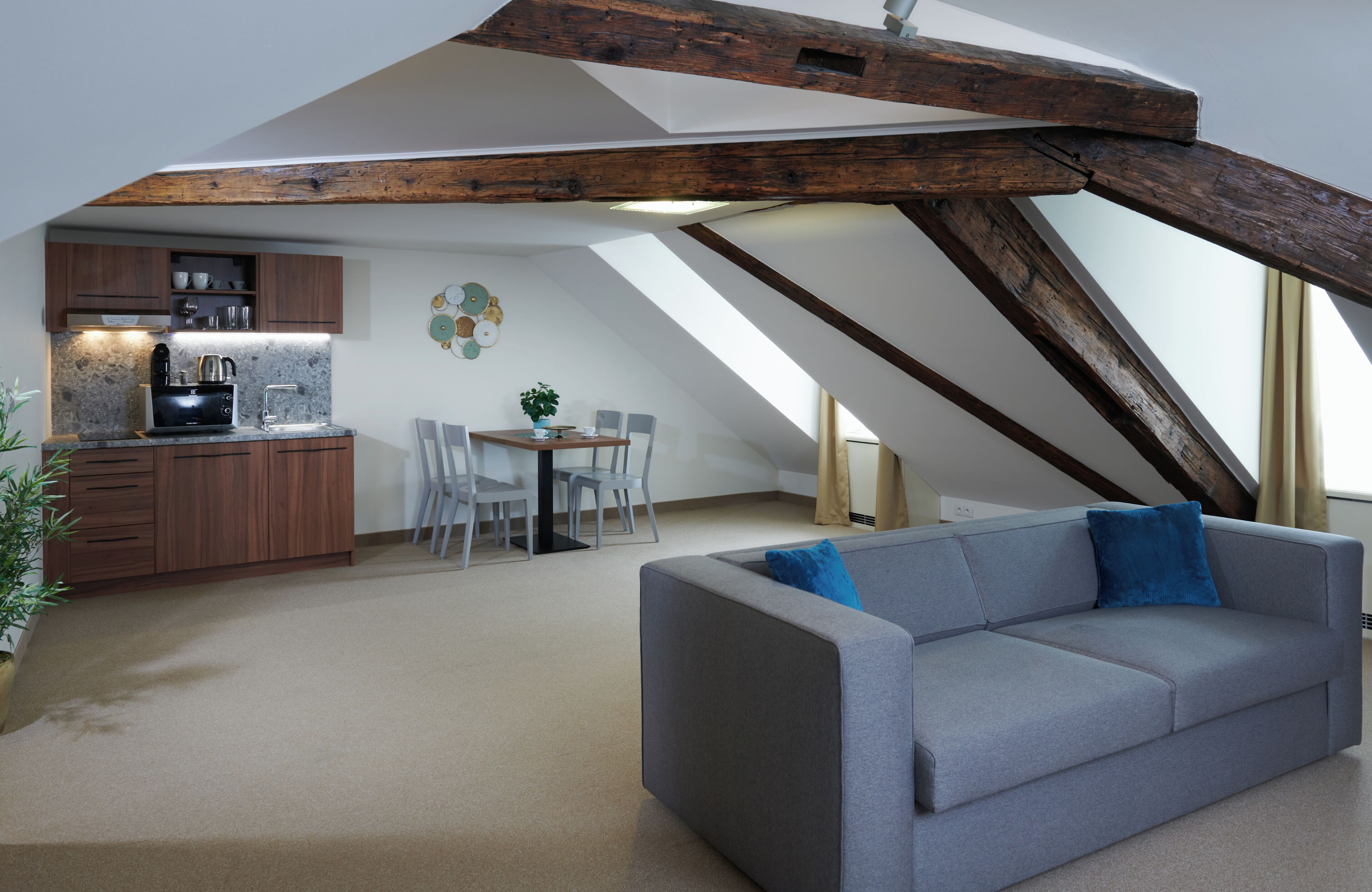 Un espacio tipo loft con cocina, comedor y un sofá gris con un cojín azul.