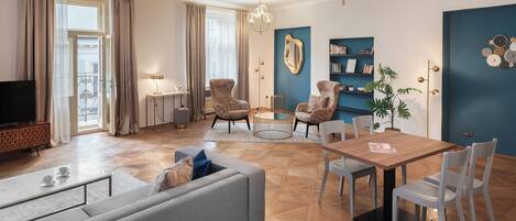 Uma sala de estar moderna com um sofá, poltronas, uma mesa de jantar com cadeiras, uma televisão e uma estante de livros.