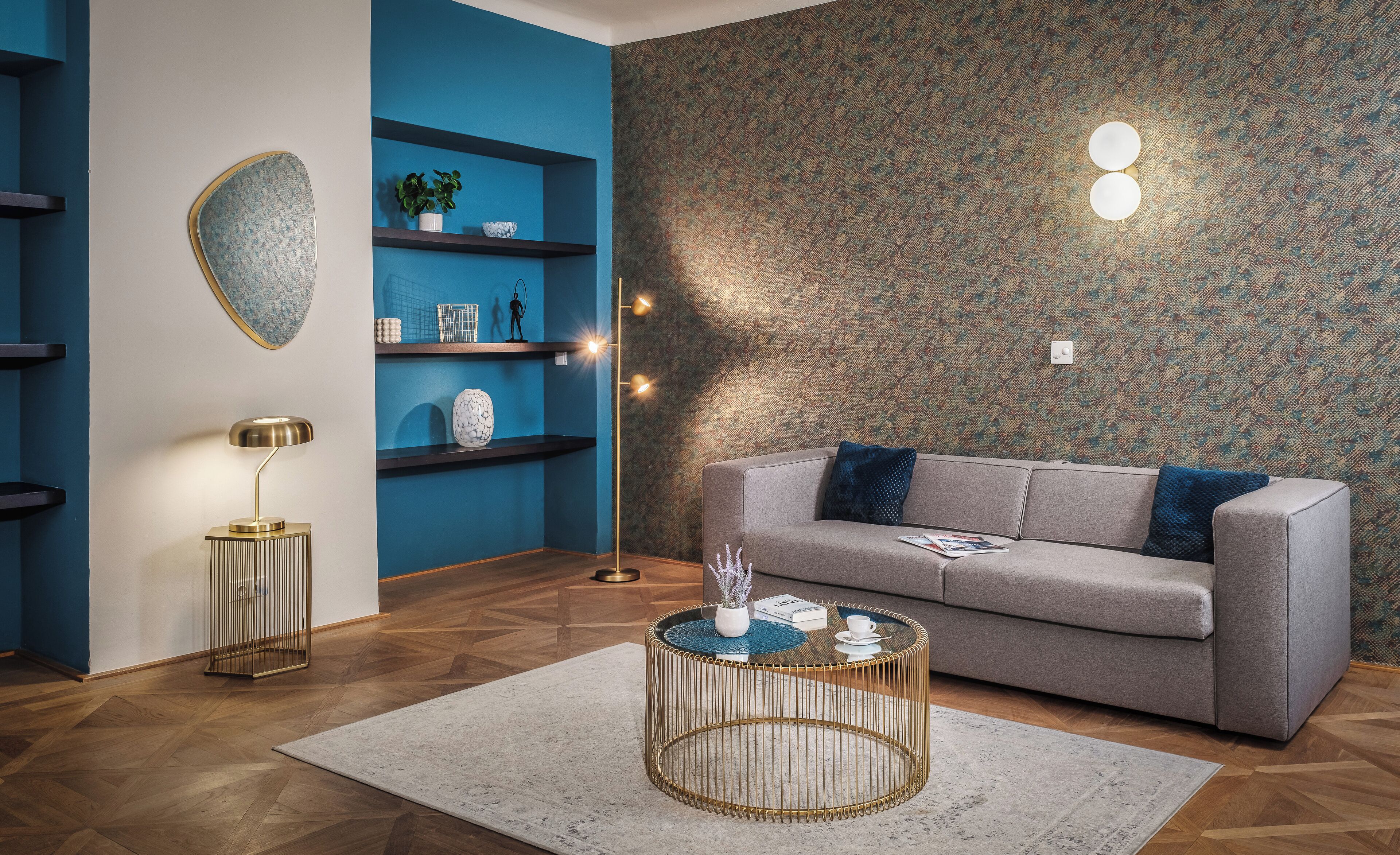 A modern living room with a grey sofa, a round coffee table, and a blue wall with shelves.