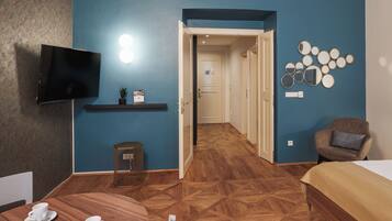 A hotel room with a TV, a small table with cups, a bed, and a hallway leading to another room.