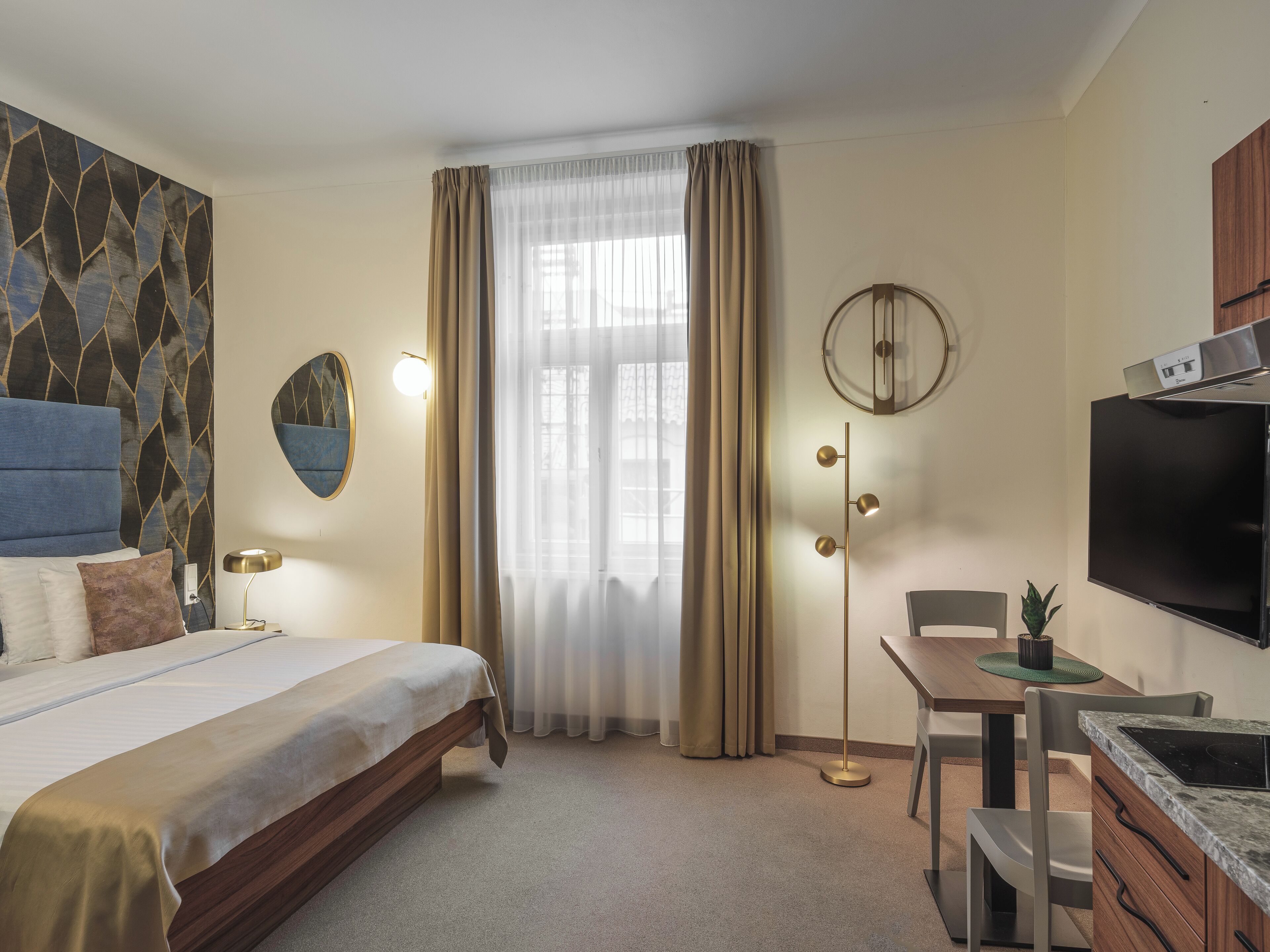 A hotel room with a bed, a desk, a chair, a TV, a clock, and a window with curtains.