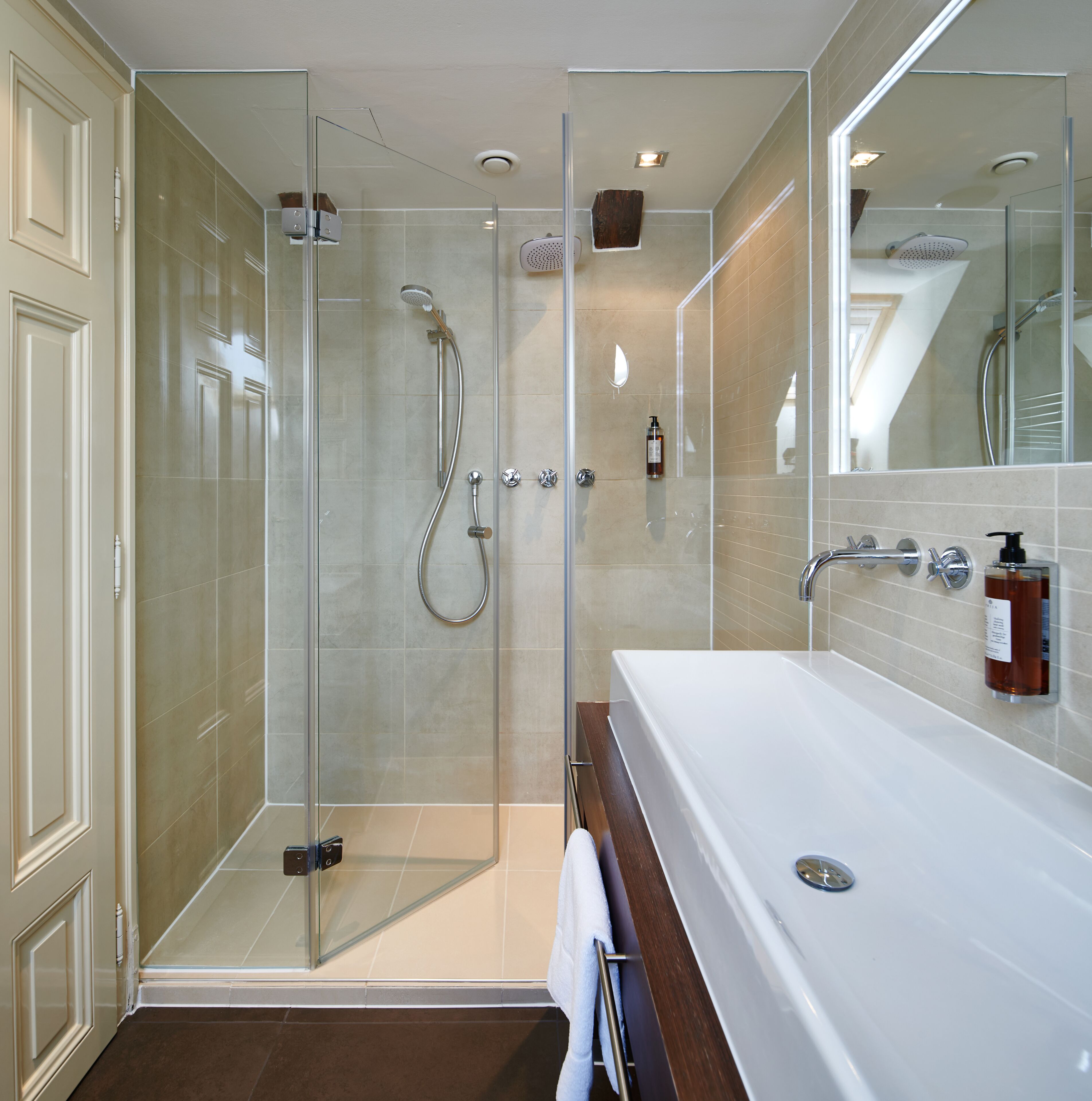 A modern bathroom with a glass-enclosed shower, a large white bathtub, and a mirror reflecting the shower area.