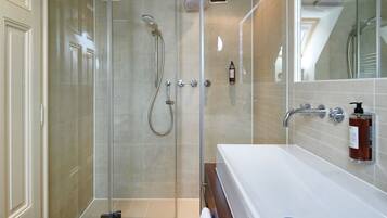 A modern bathroom with a glass-enclosed shower, a large white bathtub, and a mirror reflecting the shower area.