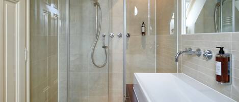 Une salle de bain moderne avec une douche à parois de verre, une grande baignoire blanche et un miroir qui reflète l’espace de la douche.