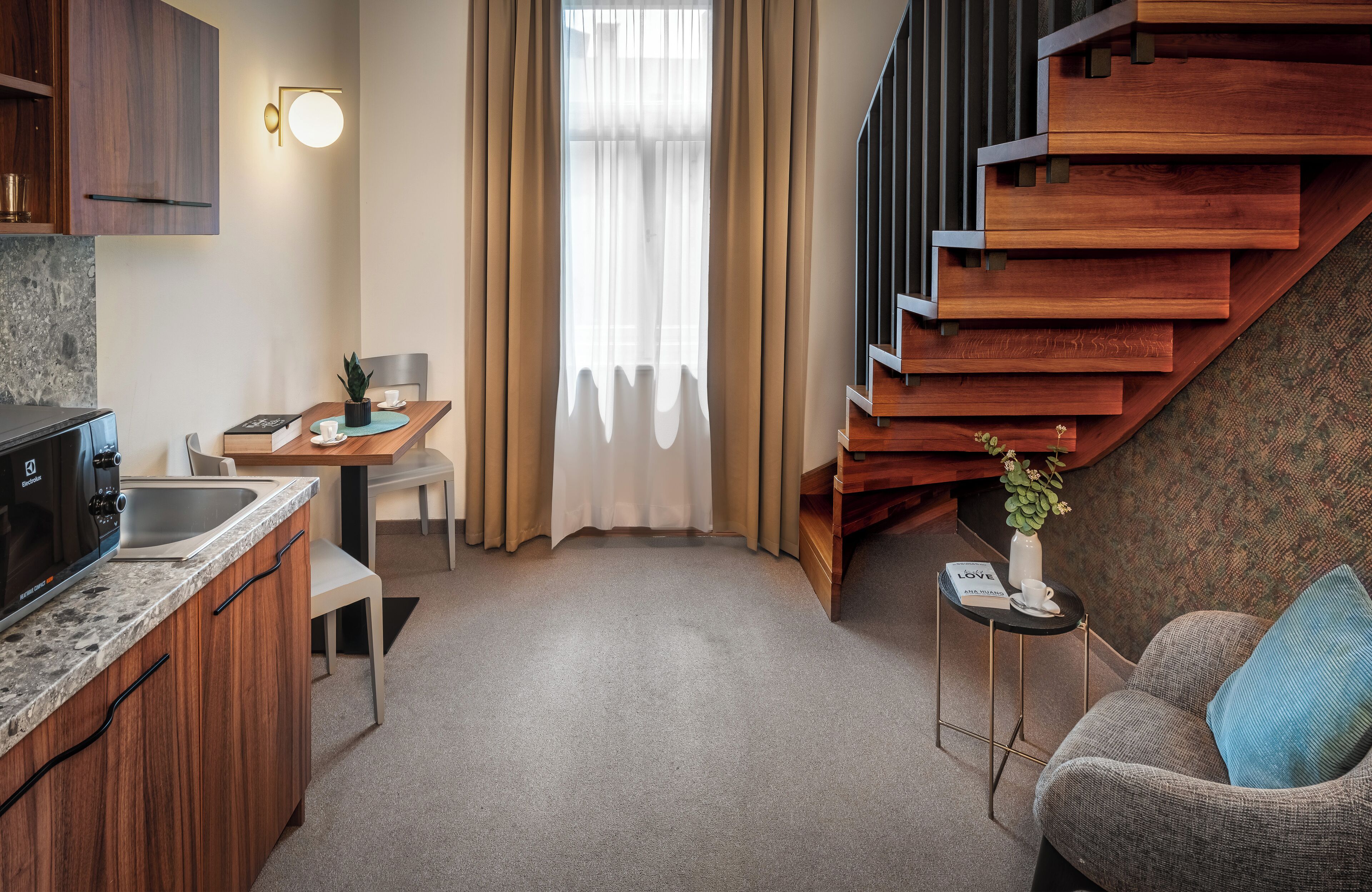 Un espacio habitable compacto con kitchenette, zona de comedor, sofá y escalera.