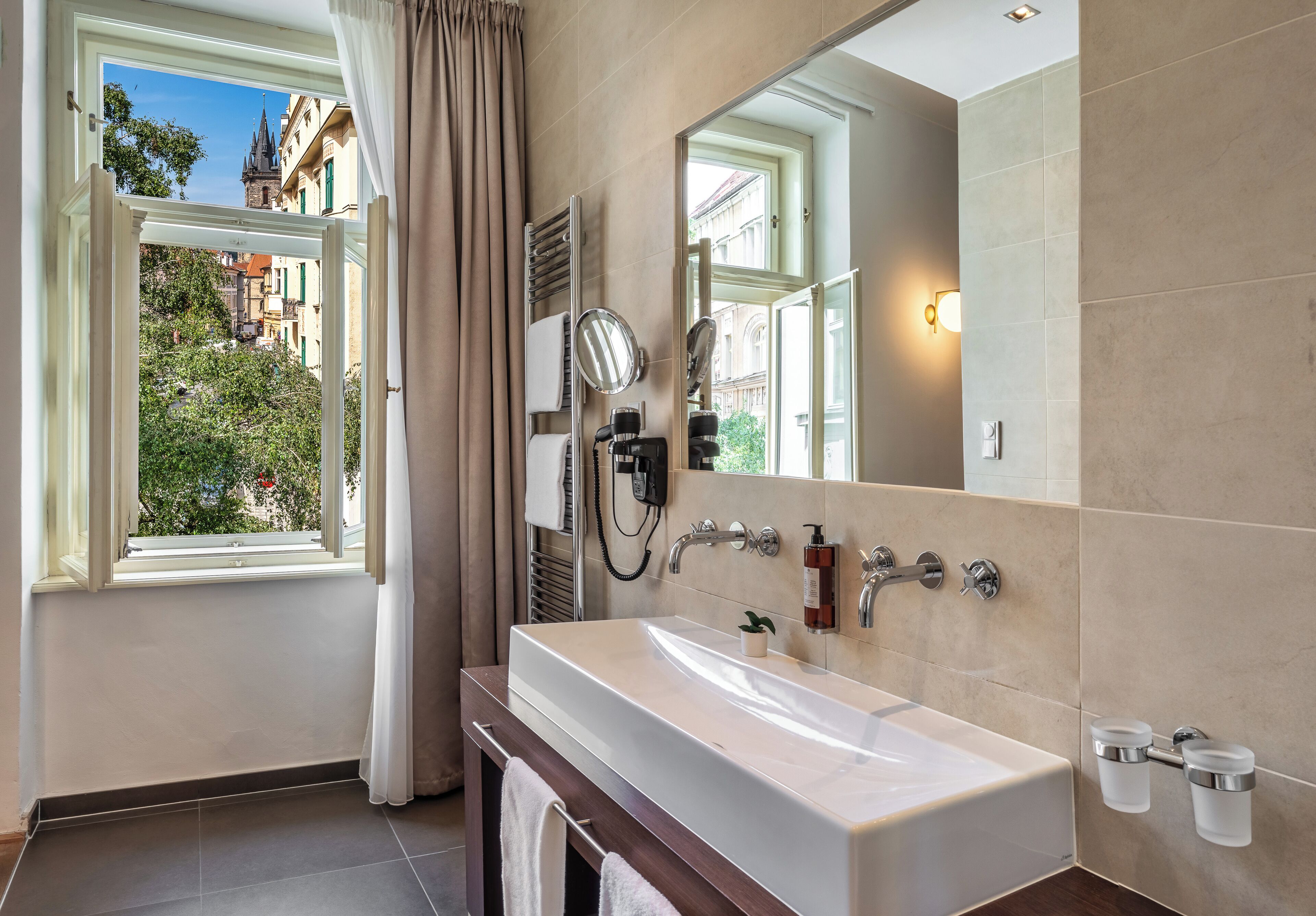 A modern bathroom with a large sink, a mirror, and a window with curtains.