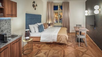Une chambre d’hôtel moderne équipée d’un lit, d’un petit coin cuisine, d’une table à manger et offrant une vue sur le paysage urbain par la fenêtre.