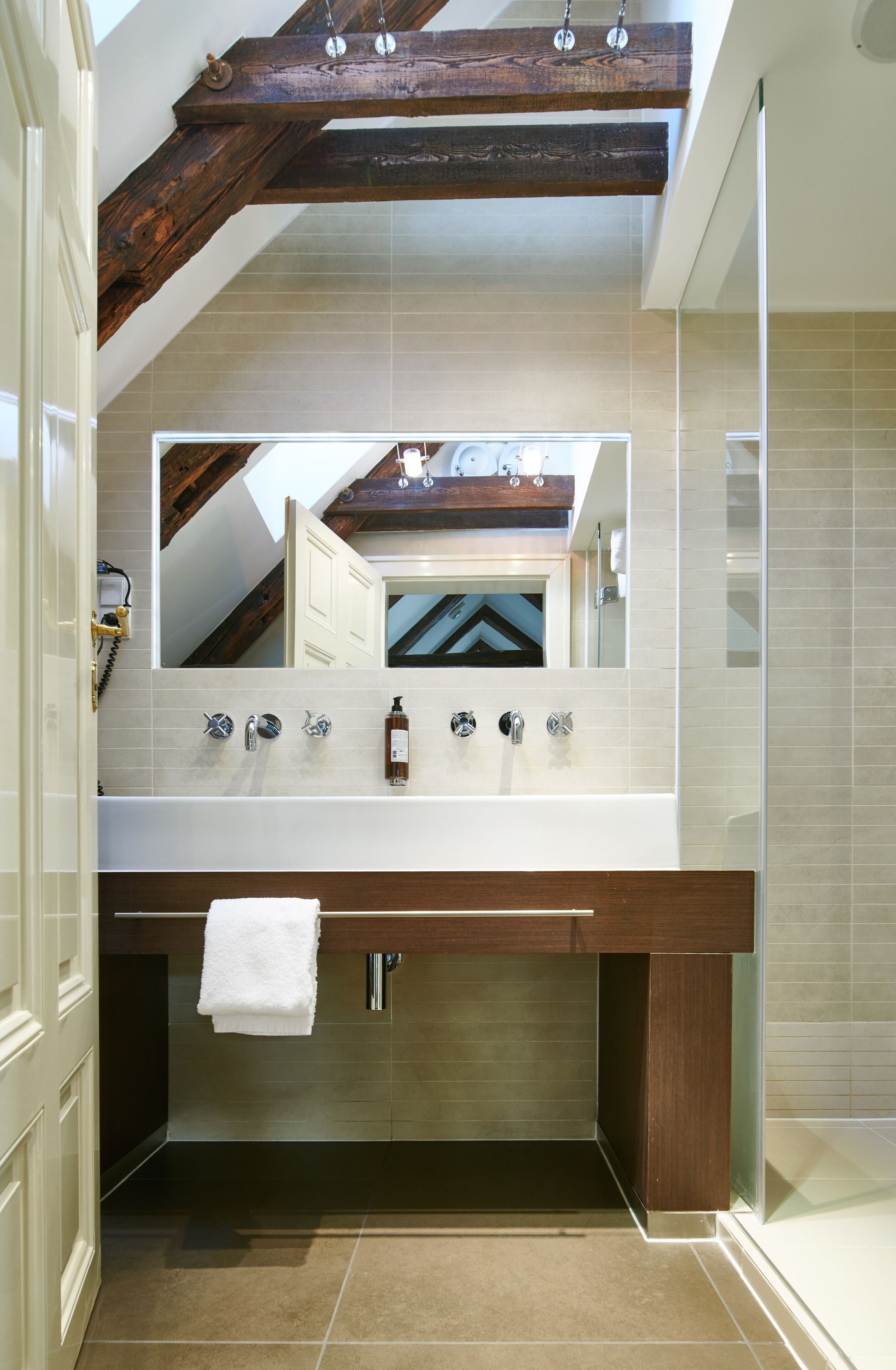 Une salle de bain moderne avec un grand miroir, une poutre en bois au plafond et une baignoire.