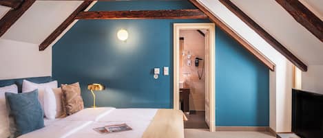 A bedroom with a bed, a bedside lamp, a TV, and a door leading to a bathroom.