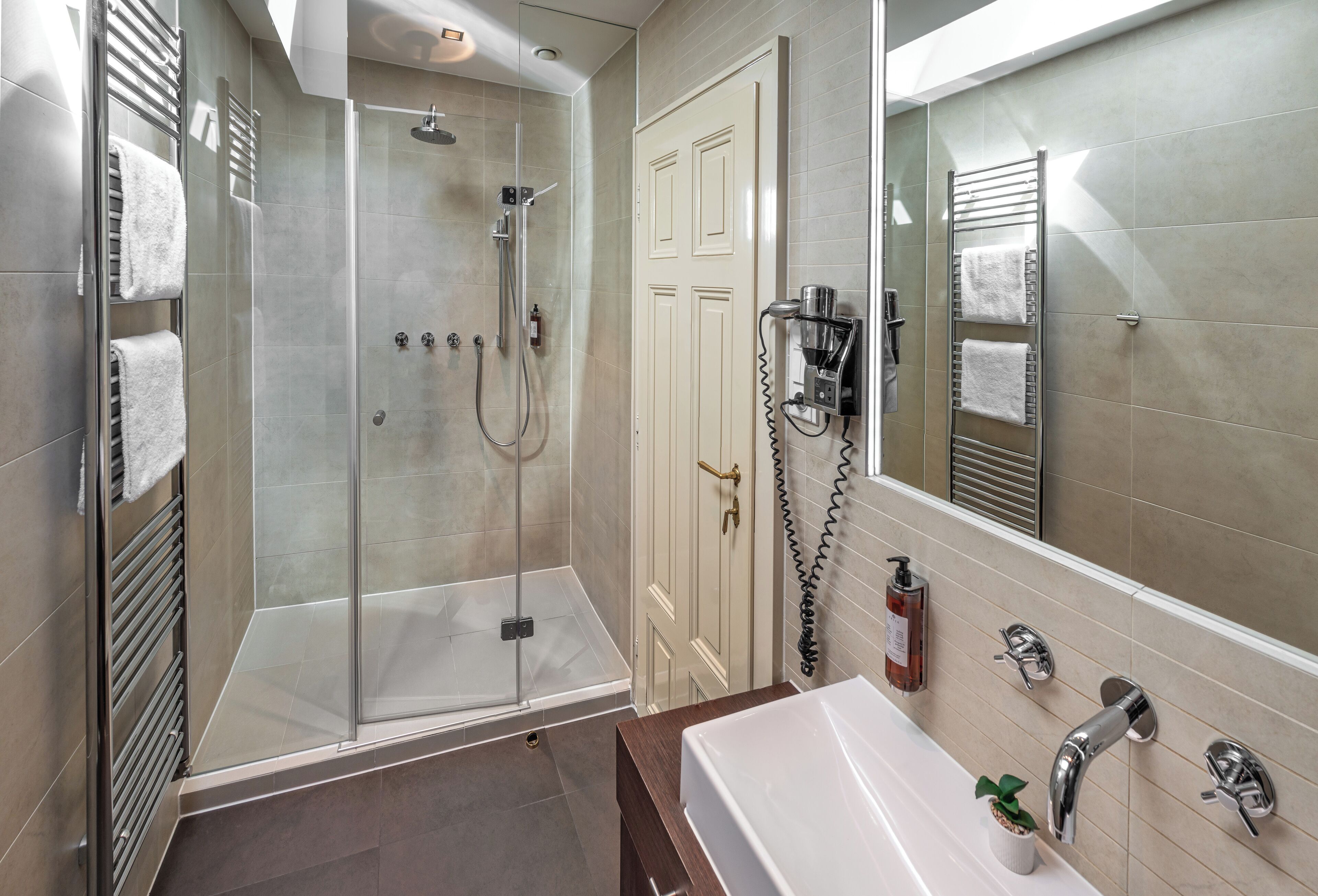 A modern bathroom with a glass-enclosed shower, a white sink, and a large mirror.