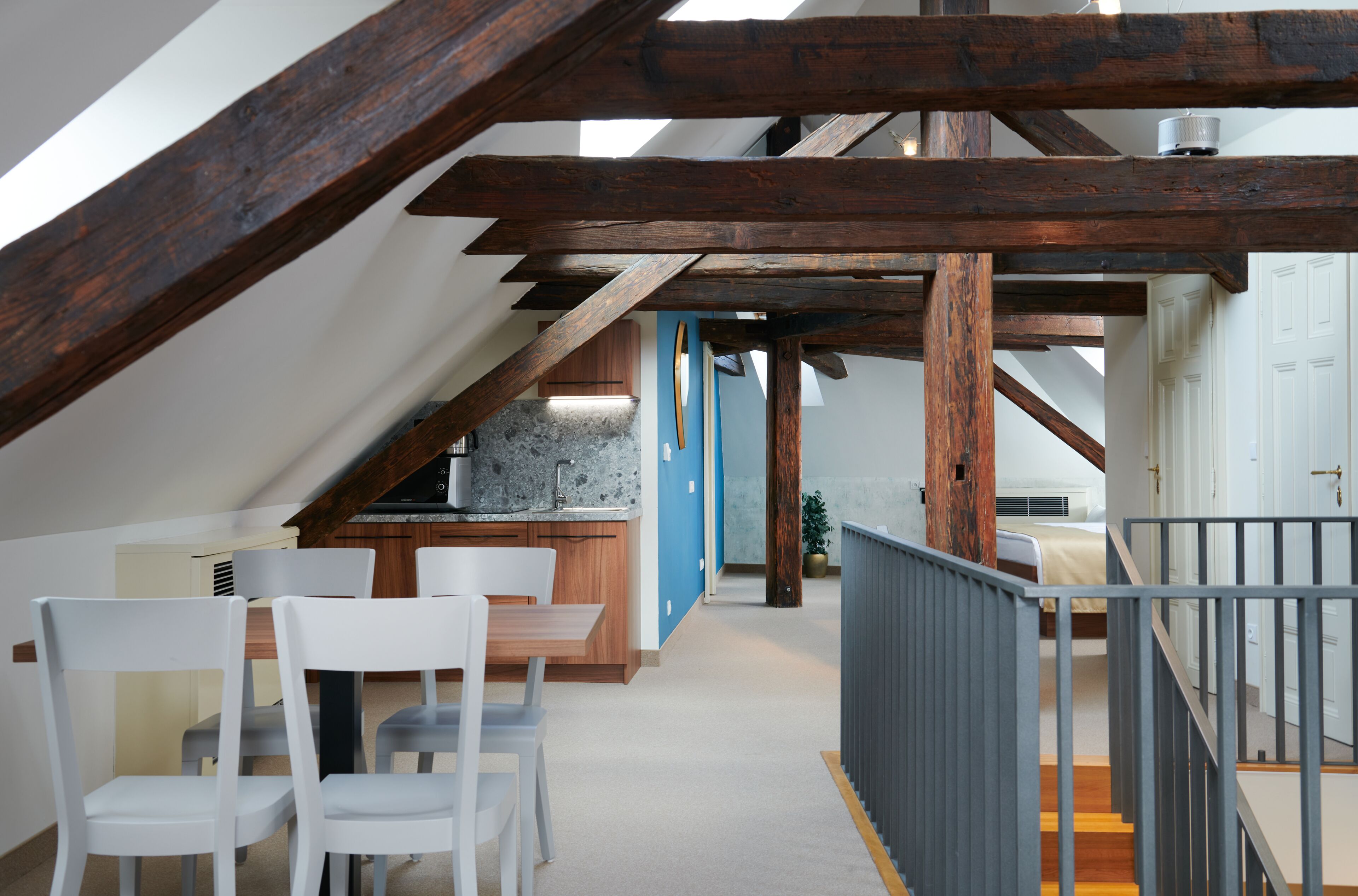 A modern interior with exposed wooden beams, a kitchen area, and a dining space with white chairs.