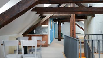 A modern interior with exposed wooden beams, a kitchen area, and a dining space with white chairs.