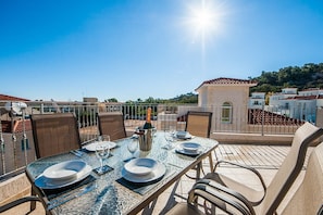 Un espace extérieur lumineux, aménagé pour les repas, avec une table dressée pour deux personnes, entourée de chaises, et offrant une vue panoramique sur une colline verdoyante.