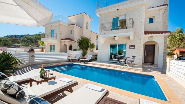 A poolside area with a pool, lounge chairs, and a table with a bottle. - Protaras holiday villa - rentprivatevillas 045 (Protaras)