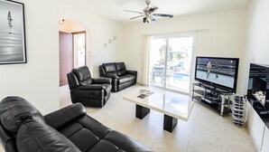 A modern living room with leather sofas, a coffee table, a TV, and a ceiling fan. - Protaras holiday villa - rentprivatevillas 045 (Protaras)