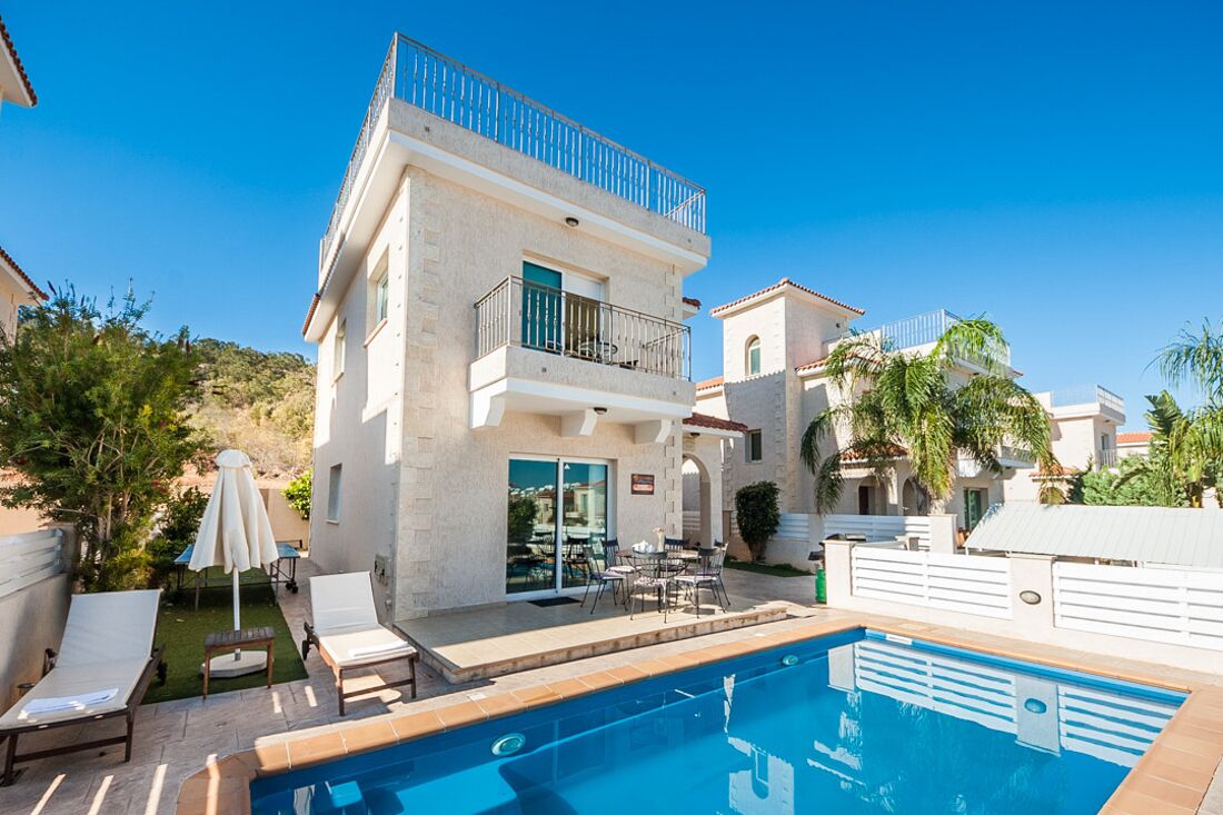 Una casa de dos pisos con piscina, mobiliario de exterior y un balcón.