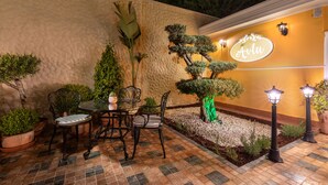 Une terrasse extérieure avec une table et des chaises, un arbre décoratif et une enseigne sur laquelle on peut lire « Avlu ».