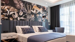Une chambre d’hôtel moderne dotée d’un grand lit, d’une tête de lit à motifs de lignes verticales, d’un bureau avec une chaise et d’une grande fenêtre avec des rideaux.