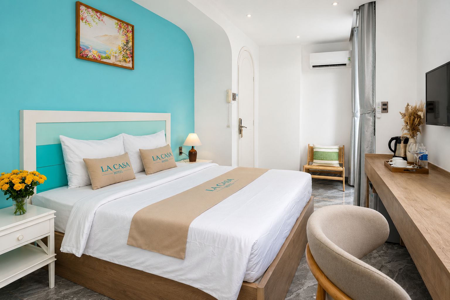 A hotel room with a bed, a desk, a chair, a TV, and a painting on the wall.
