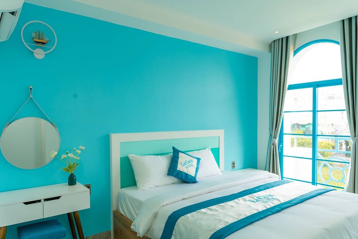A hotel room with a large bed, a bedside table with a mirror, and a window with curtains.