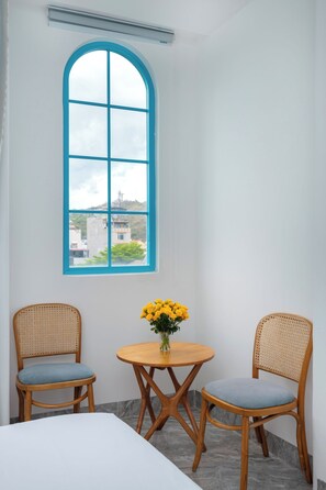 A room with a large arched window, two wicker chairs, a small wooden table, and a vase of yellow flowers. - La Casa Hotel (Ho Chi Minh City)