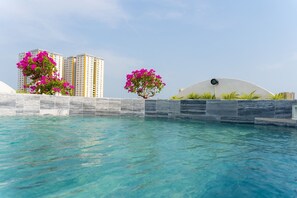 A swimming pool with clear blue water, surrounded by a stone wall and two pink flowering trees. - La Casa Hotel (Ho Chi Minh City)