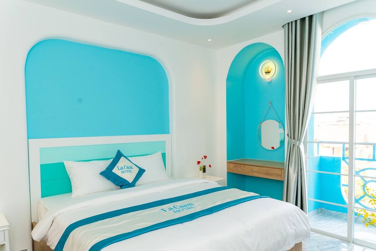 A hotel room with a bed, a nightstand, a mirror, and a window with curtains.
