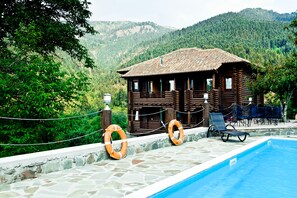 A wooden cabin with a swimming pool, surrounded by lush greenery and mountains. - Yliessa Chalet (Karpenisi)