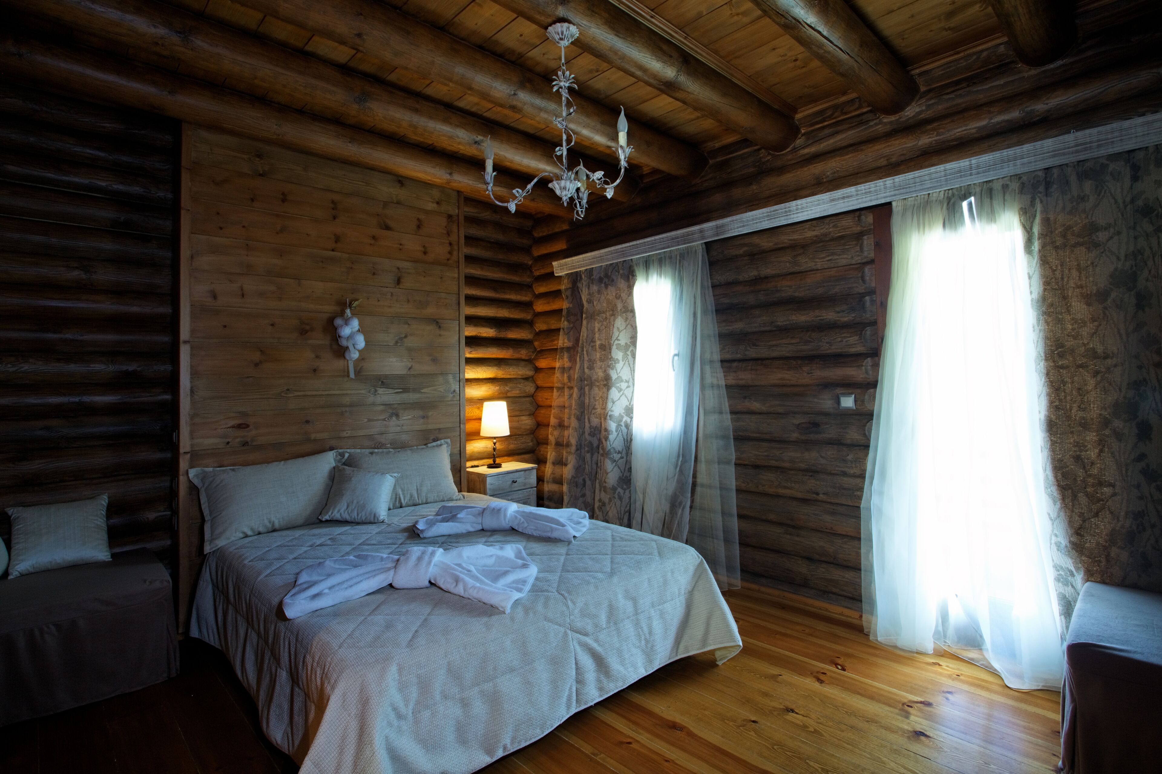 Un dormitorio tipo cabaña de troncos con una cama grande, una mesita de noche con lámpara y un candelabro.