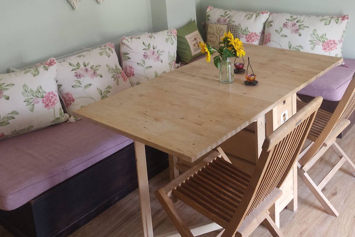 A dining area with a wooden table and benches, floral cushions, and wall decorations.