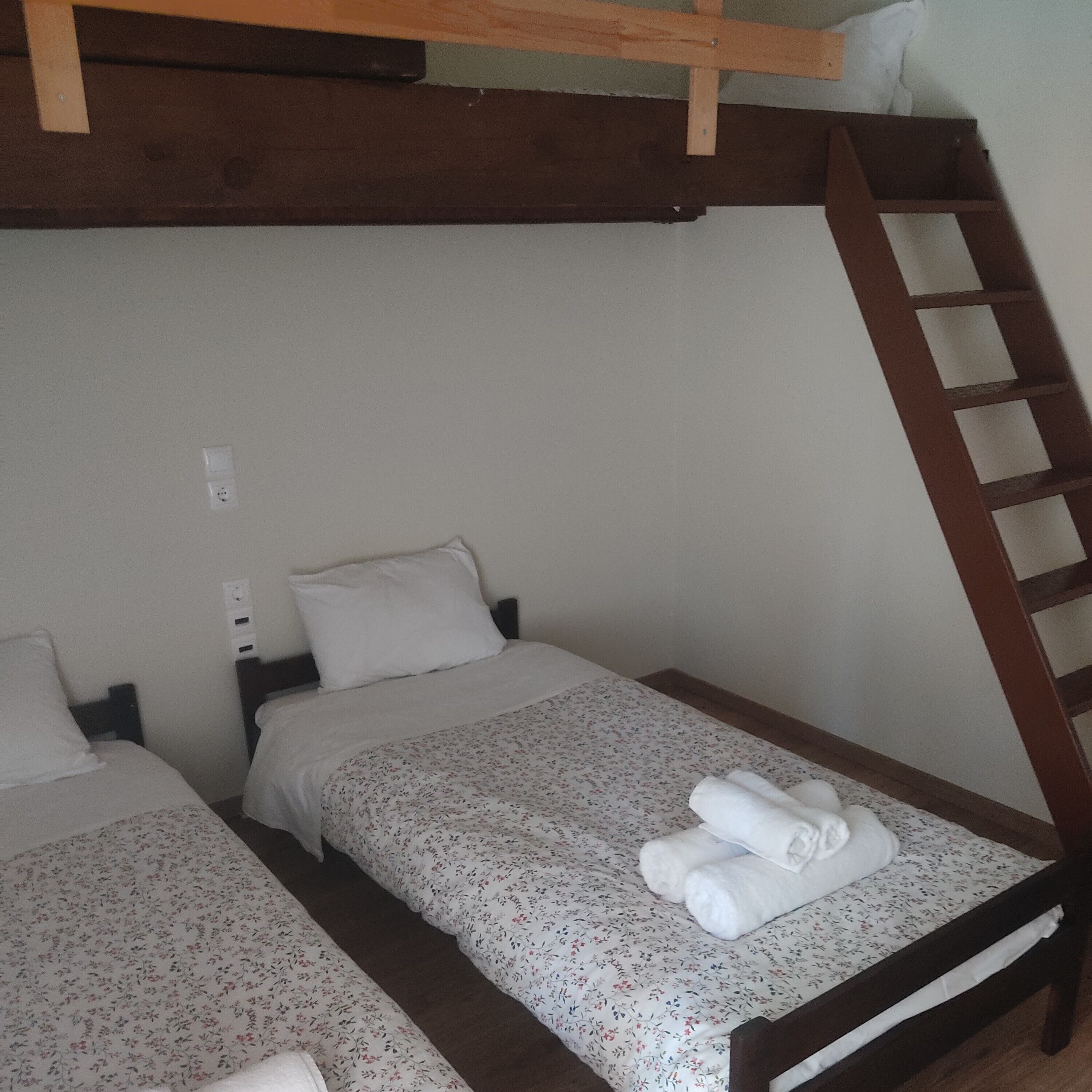 Een kamer met twee eenpersoonsbedden, elk met een houten hoofdbord en een bloemenprint sprei. Er is een houten ladder aan de muur bevestigd, en een wit kussen op een van de bedden.