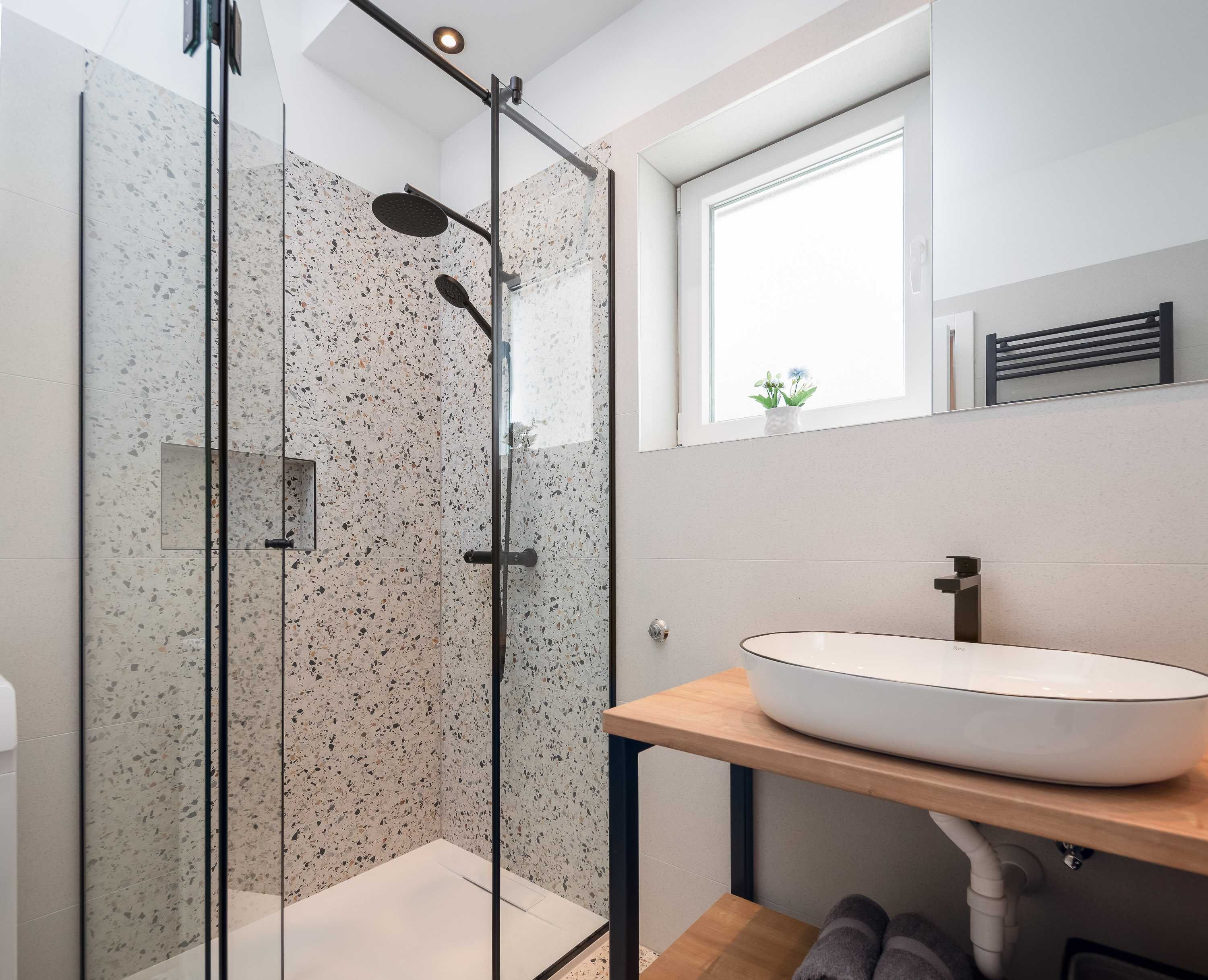Une salle de bain moderne avec une douche à parois de verre, un lavabo blanc doté d’un plan de toilette en bois et une fenêtre située au-dessus du lavabo.