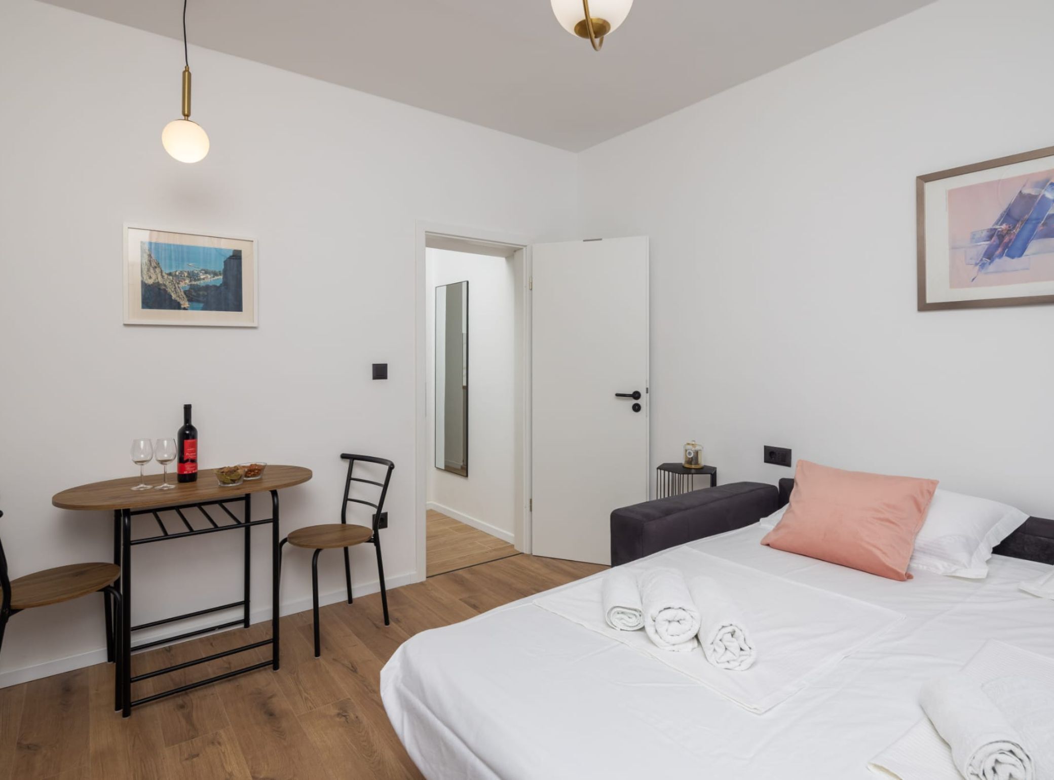 A hotel room with a bed, a small table with a chair, a wine bottle, and a framed picture on the wall.